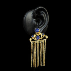 Exuding a regal aura, these earrings showcase a crown-like gold motif adorned with deep blue gemstones and cascading gold chains. The intricate detailing adds to their luxurious appeal.